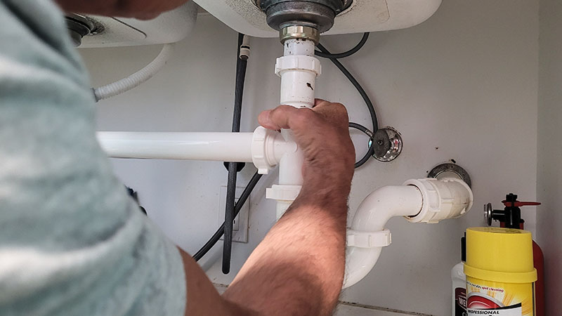 plumber reconnecting pvc drain pipe after burst pipe repair under sink