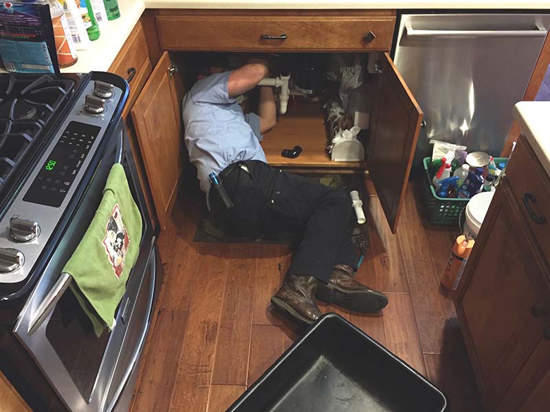 plumber performing emergency burst pipe repair under kitchen sink cabinet