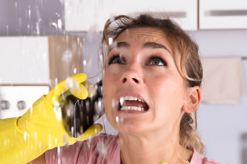 panicked homeowner calling emergency plumber while water sprays from burst pipe