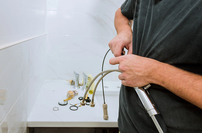 Plumber Installing Faucet Supply Lines at Bathroom Sink plumber connecting braided supply lines during faucet repair at bathroom sink