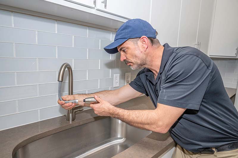 Plumber Tightening Kitchen Faucet Fitting at Sink plumber tightening kitchen faucet fitting at stainless sink with wrench