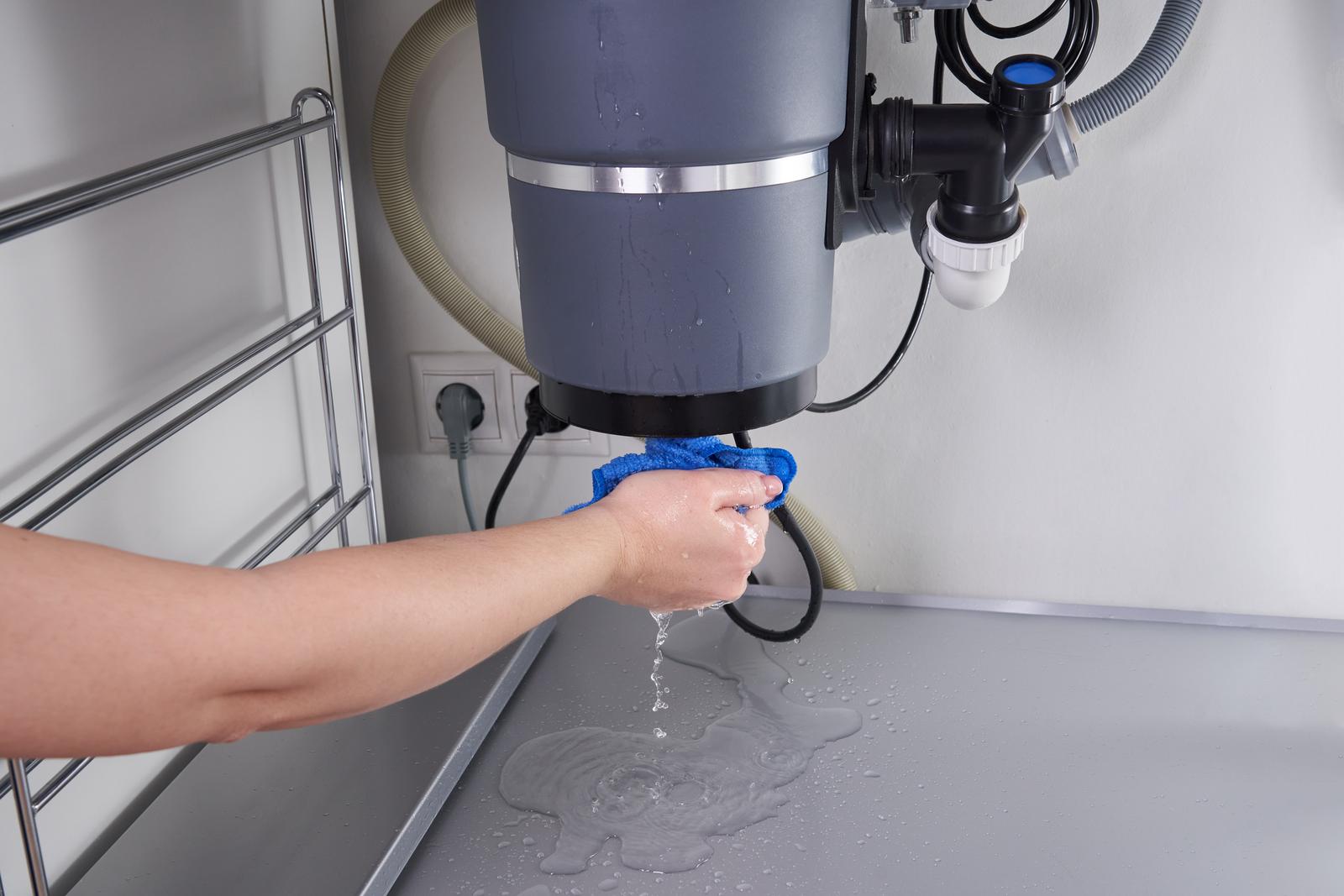 Leaking Garbage Disposal Unit Being Wiped Under Sink hand wiping water leak from garbage disposal unit under sink