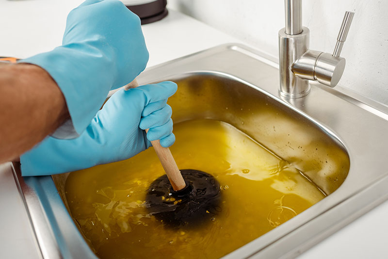 Plumber Using Plunger on Clogged Kitchen Sink plumber in rubber gloves using plunger to clear clogged sink drain