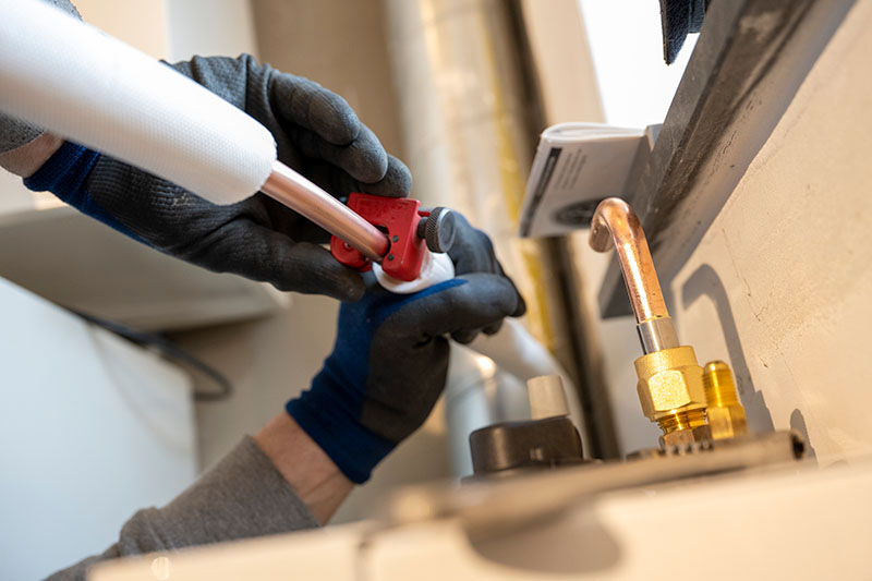 plumber in gloves cutting copper pipe with pipe cutter during repiping service