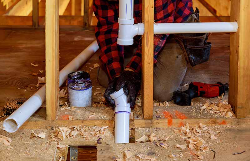 New PVC Sewer Pipe System Installation in Floor Framing plumber installing new pvc sewer pipe system through floor framing during replacement