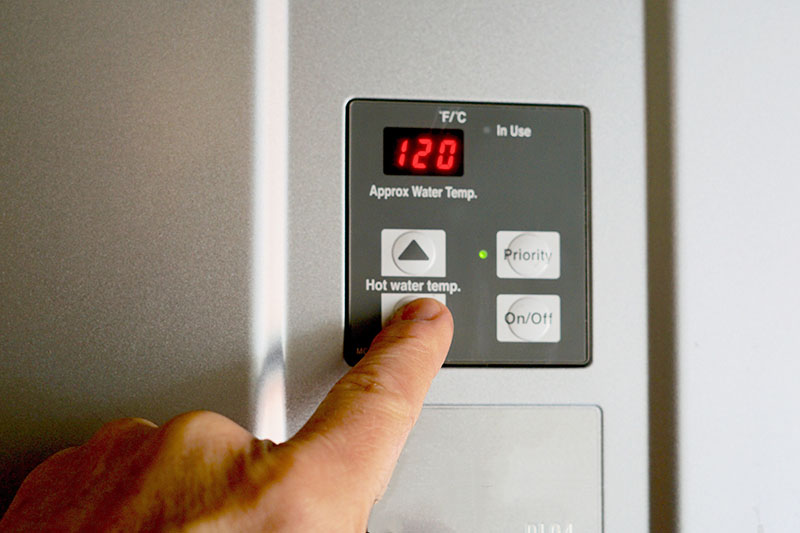 finger adjusting tankless water heater temperature display set to 120 degrees