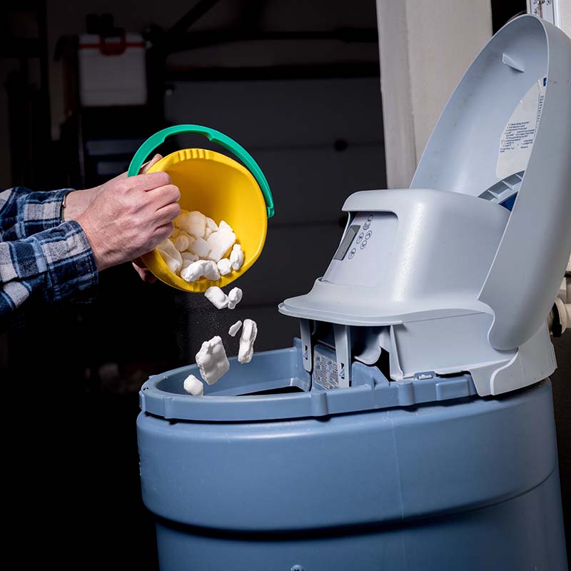 Adding Salt to Water Softener Brine Tank hand pouring salt pellets into water softener brine tank