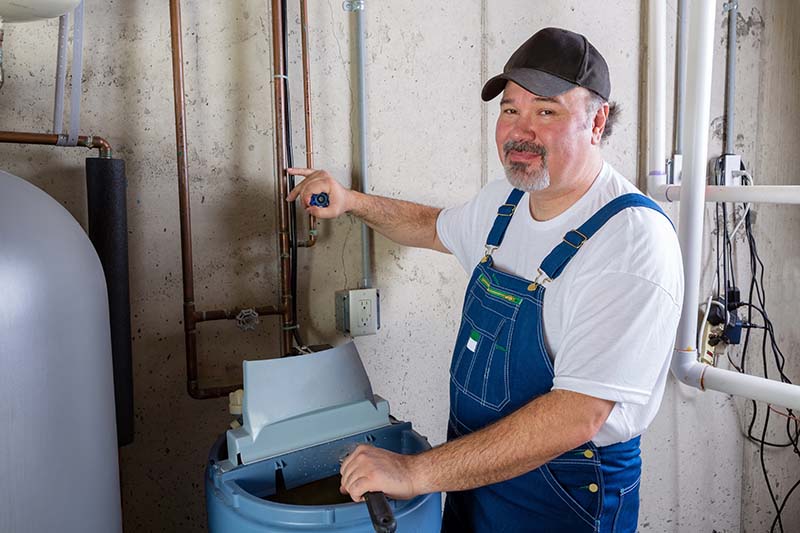 Plumber Servicing Water Softener System in Utility Room plumber in overalls servicing water softener system in utility room